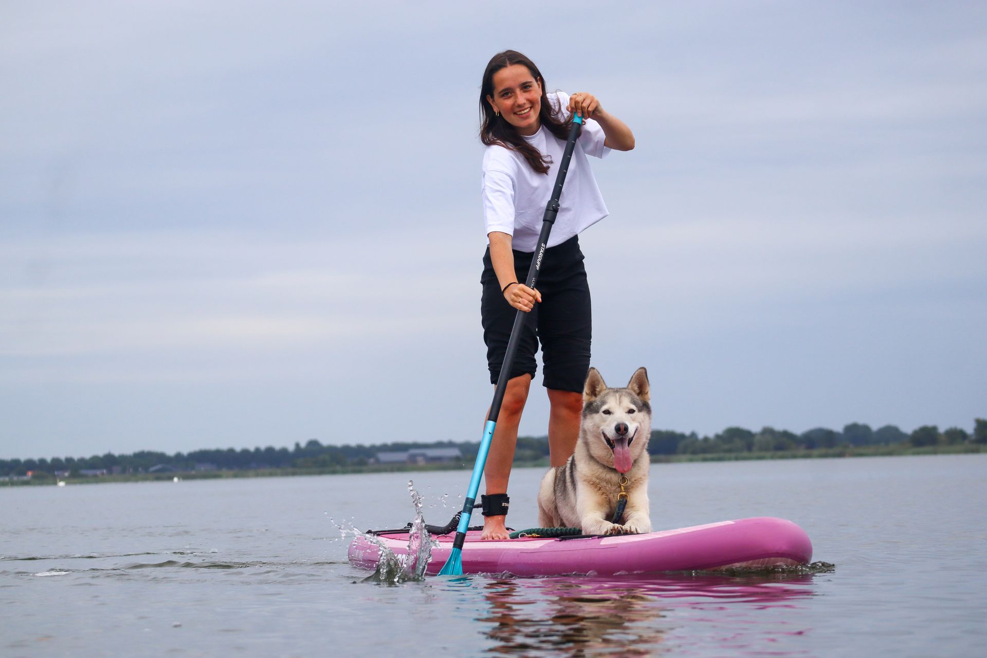 Een vrouw en haar hond zitten op een roze paddleboard