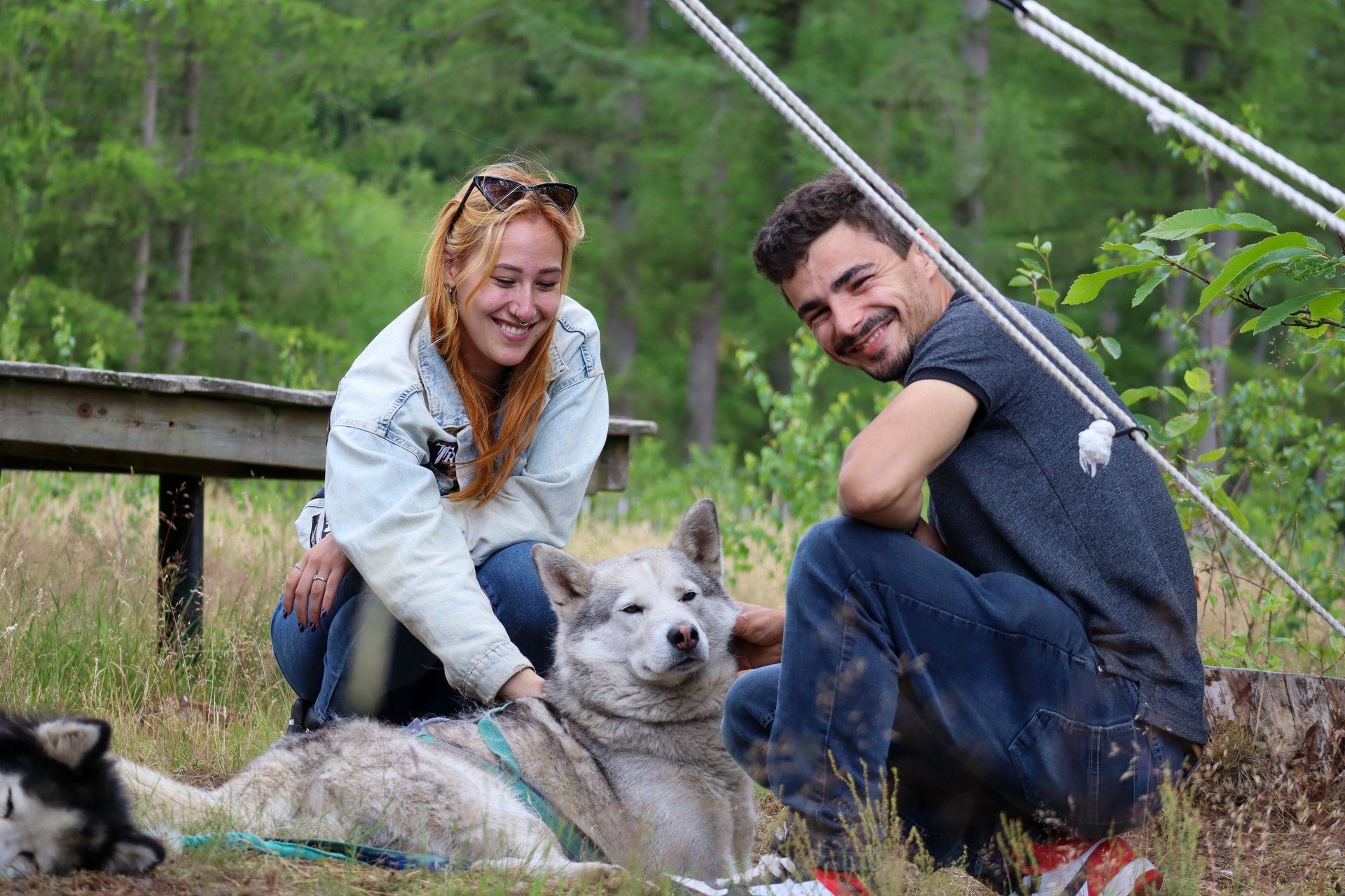 Vrouw en man aaien buiten een husky; beiden lachen.