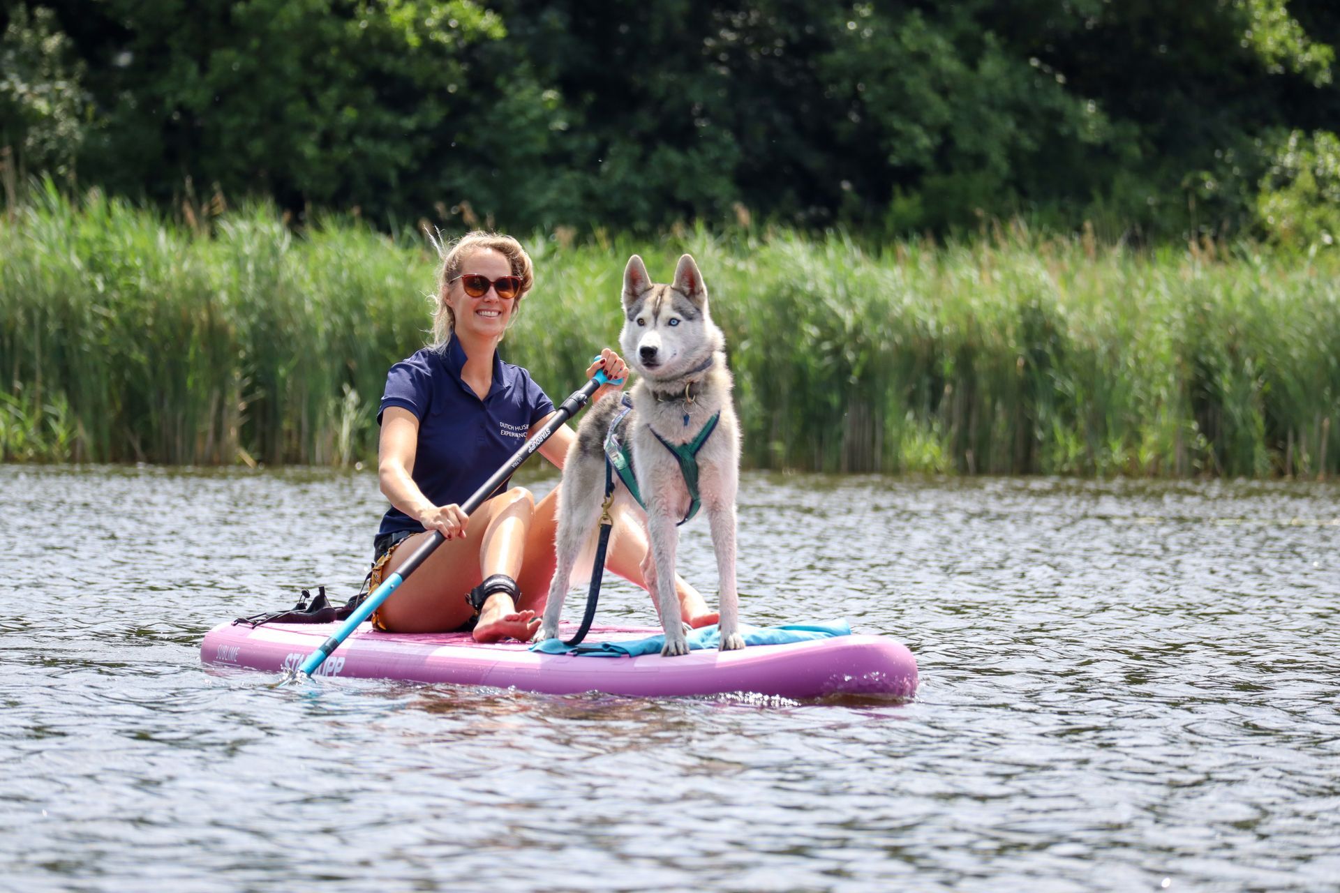 Een vrouw zit met haar hond op een paddleboard