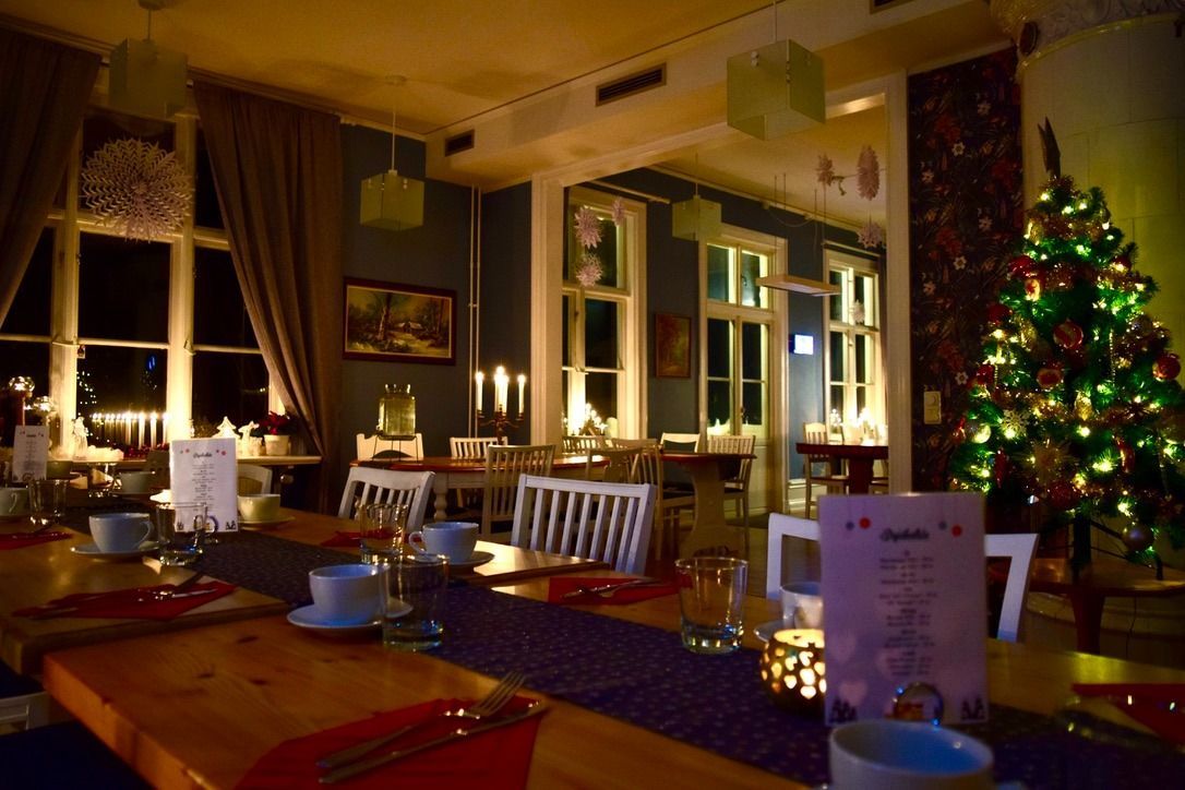 Gezellige eetkamer versierd voor Kerstmis, met verlichte kerstboom, gedekte tafels en ramen met uitzicht op de nacht.