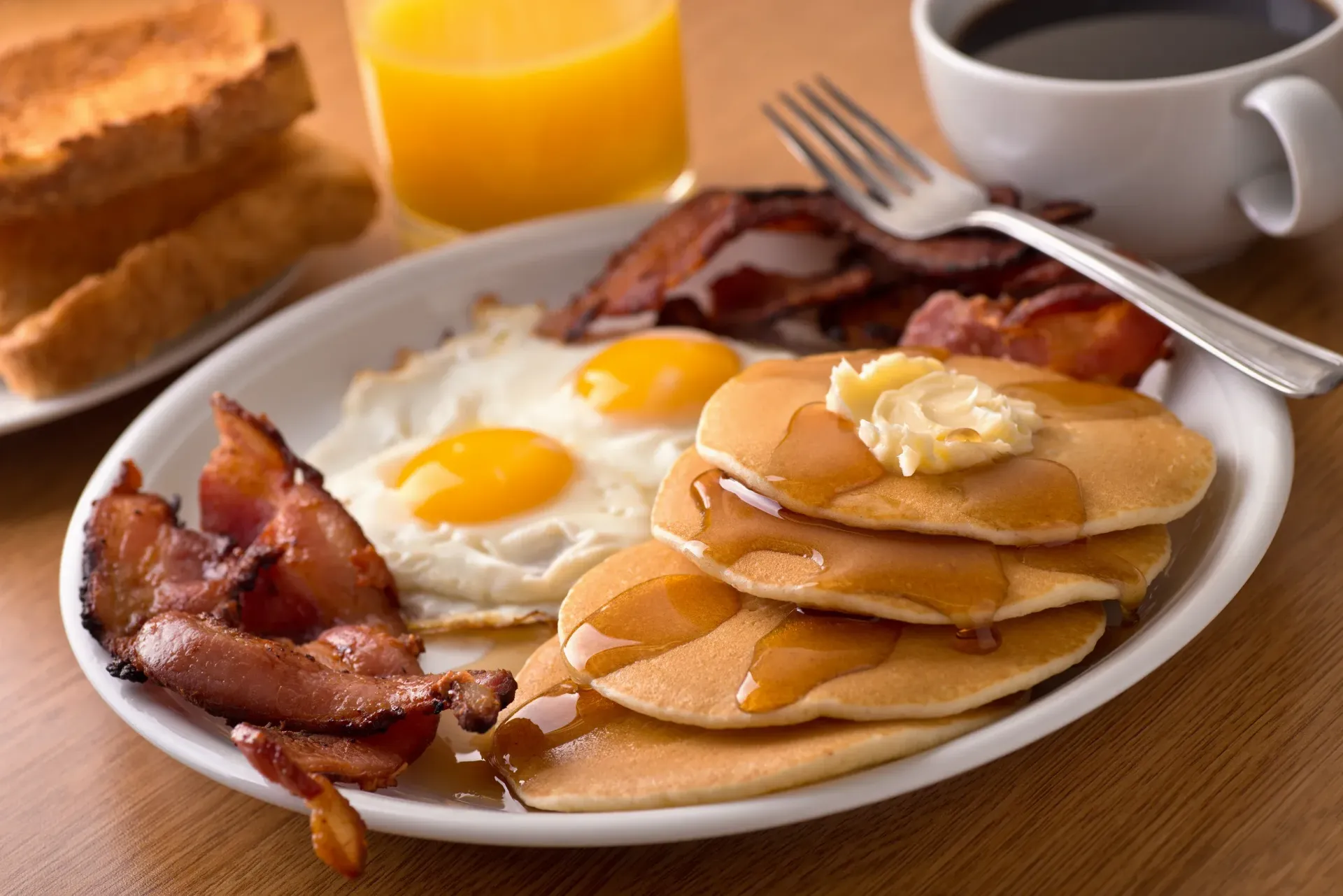 A white plate topped with pancakes eggs bacon and syrup