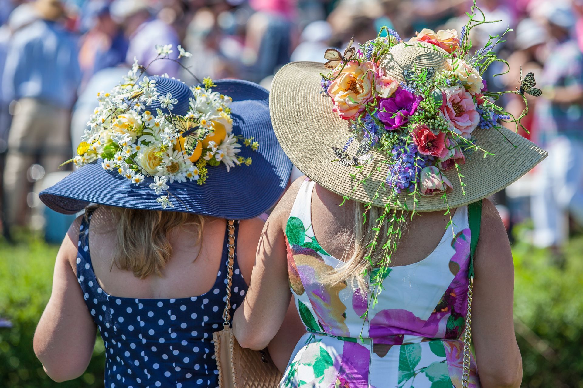 Two women wearing hats decorated with flowers are standing next to each other.