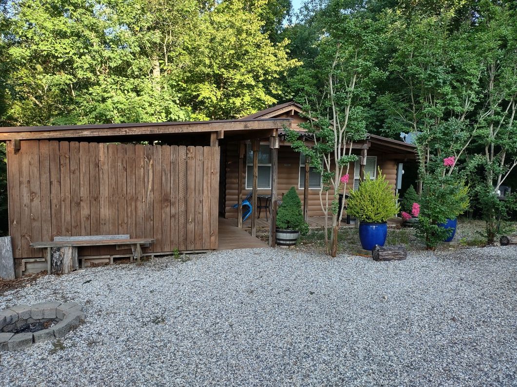 A small wooden house is surrounded by trees and gravel.