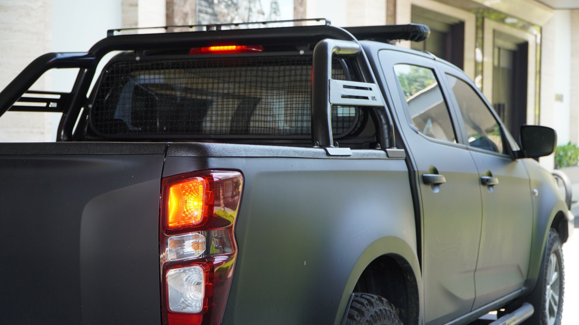 Gray pickup truck parked under a covered driveway, rear view with taillights and cargo rack visible.