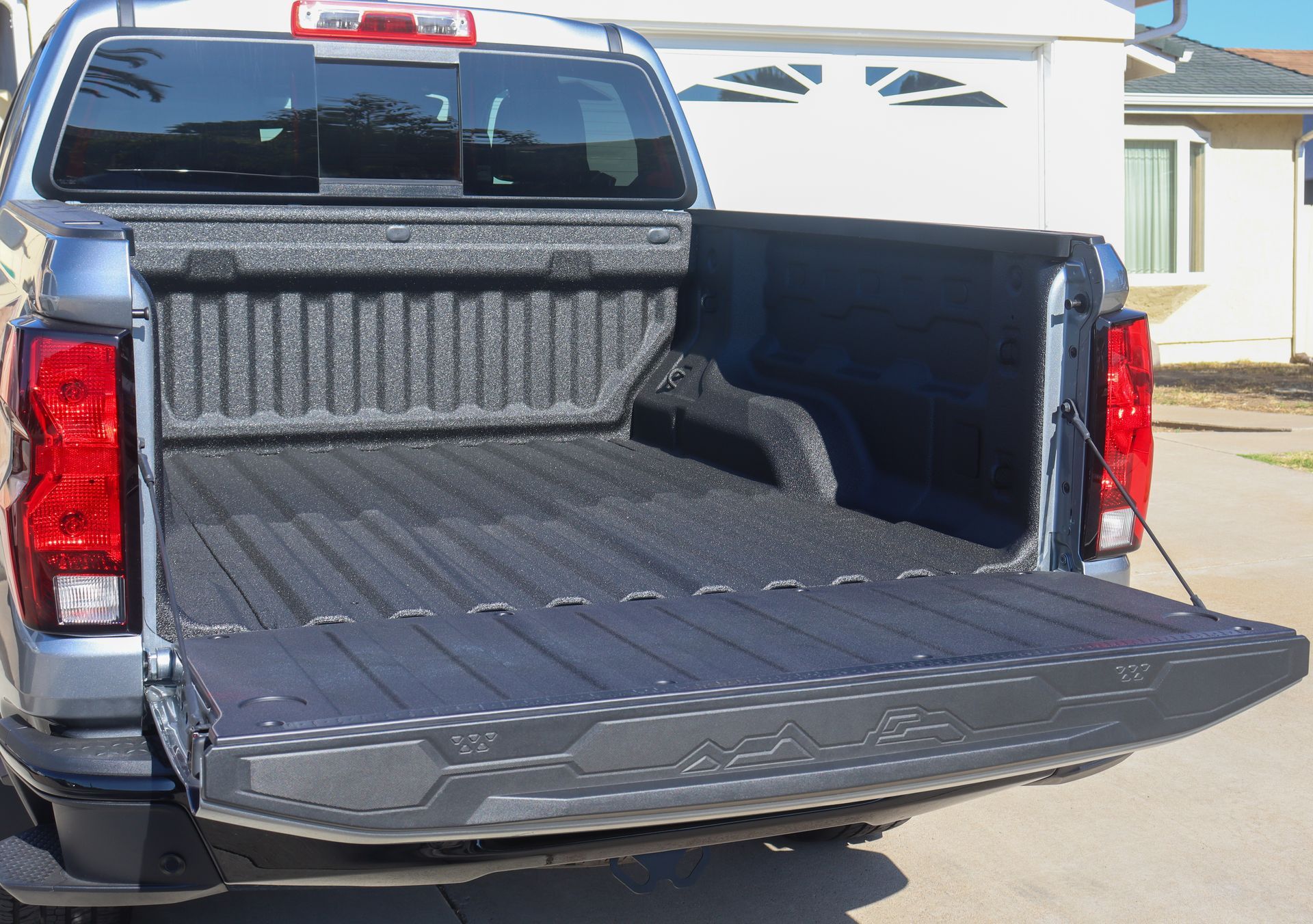 Pickup truck bed with tailgate lowered and bed liner visible, parked outside a house.