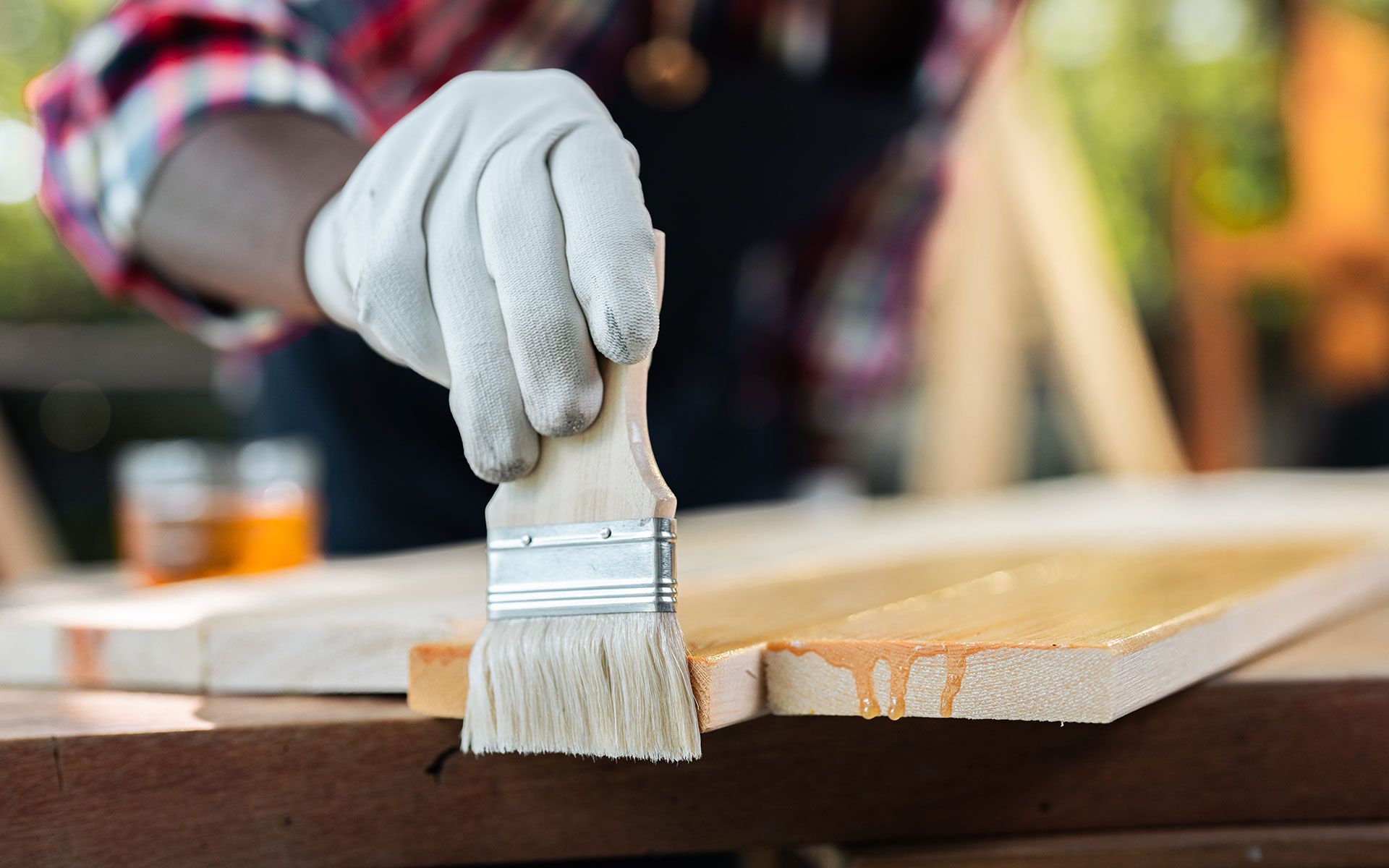 Person in gloves brushing varnish onto wooden surface.