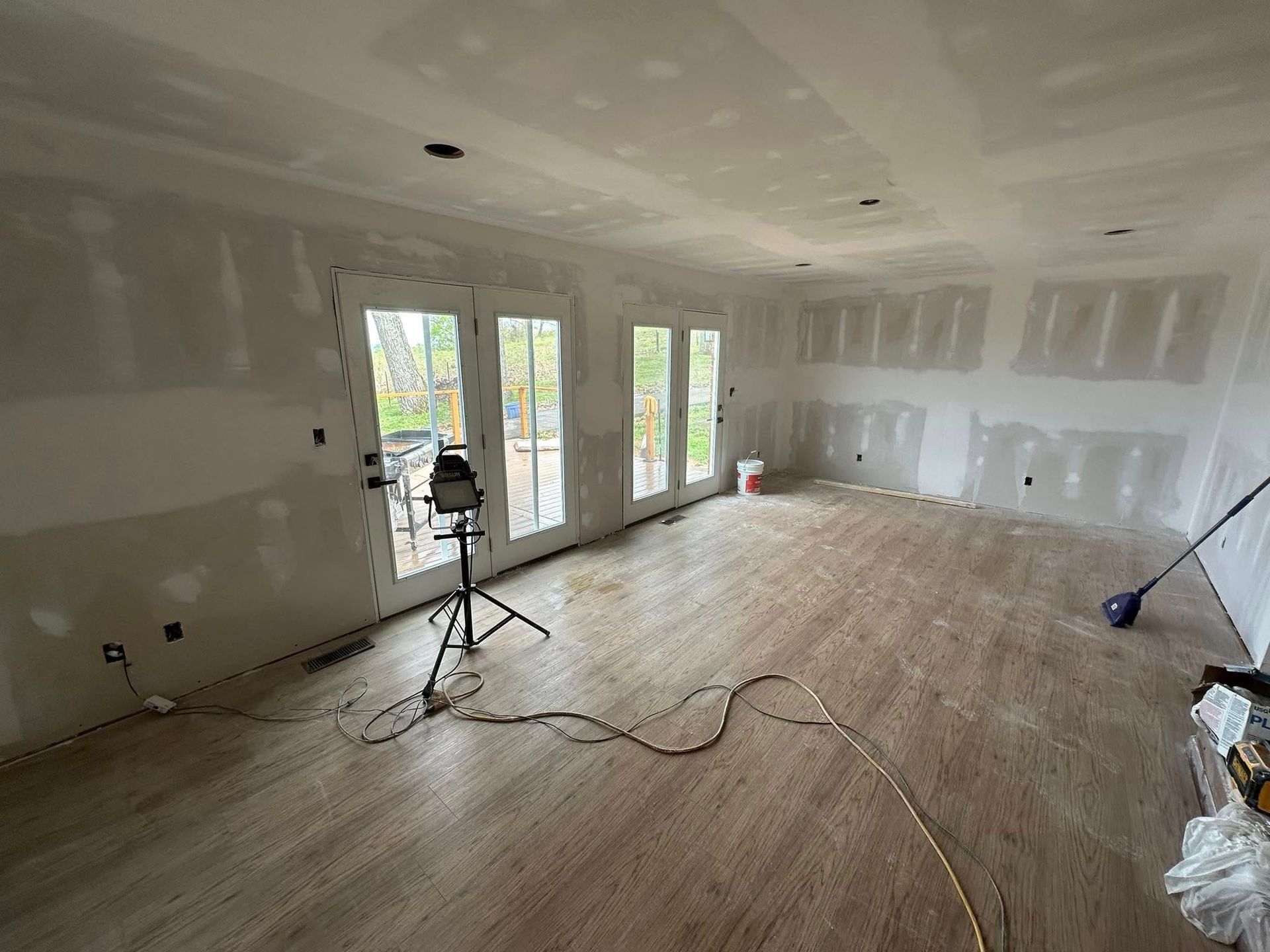 Person painting a wall tan in a light-filled living room with a ladder, fireplace, and furniture.