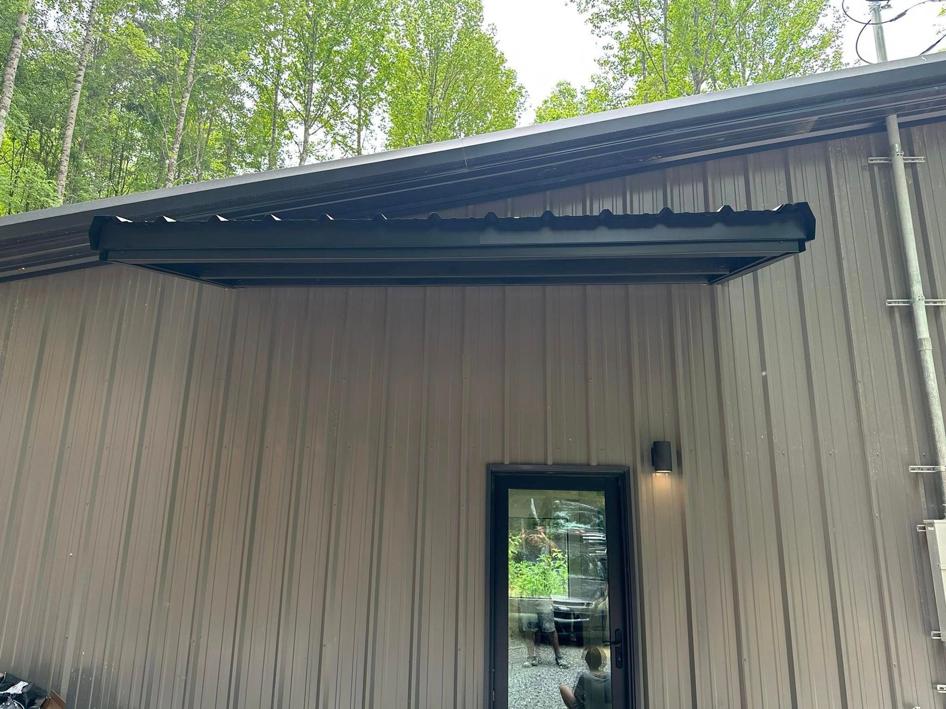 Person paints a weathered barn, standing on the ground with a ladder, applying dark paint to light blue siding.