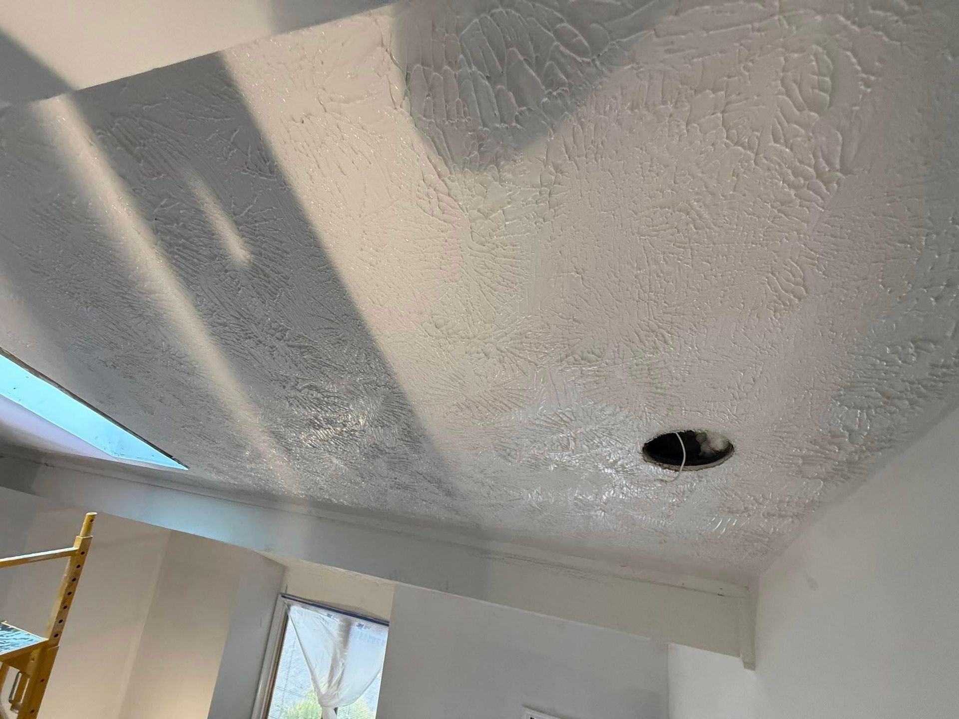 Man installing drywall on a ceiling using a drill. White, gray, and metallic materials in a room.