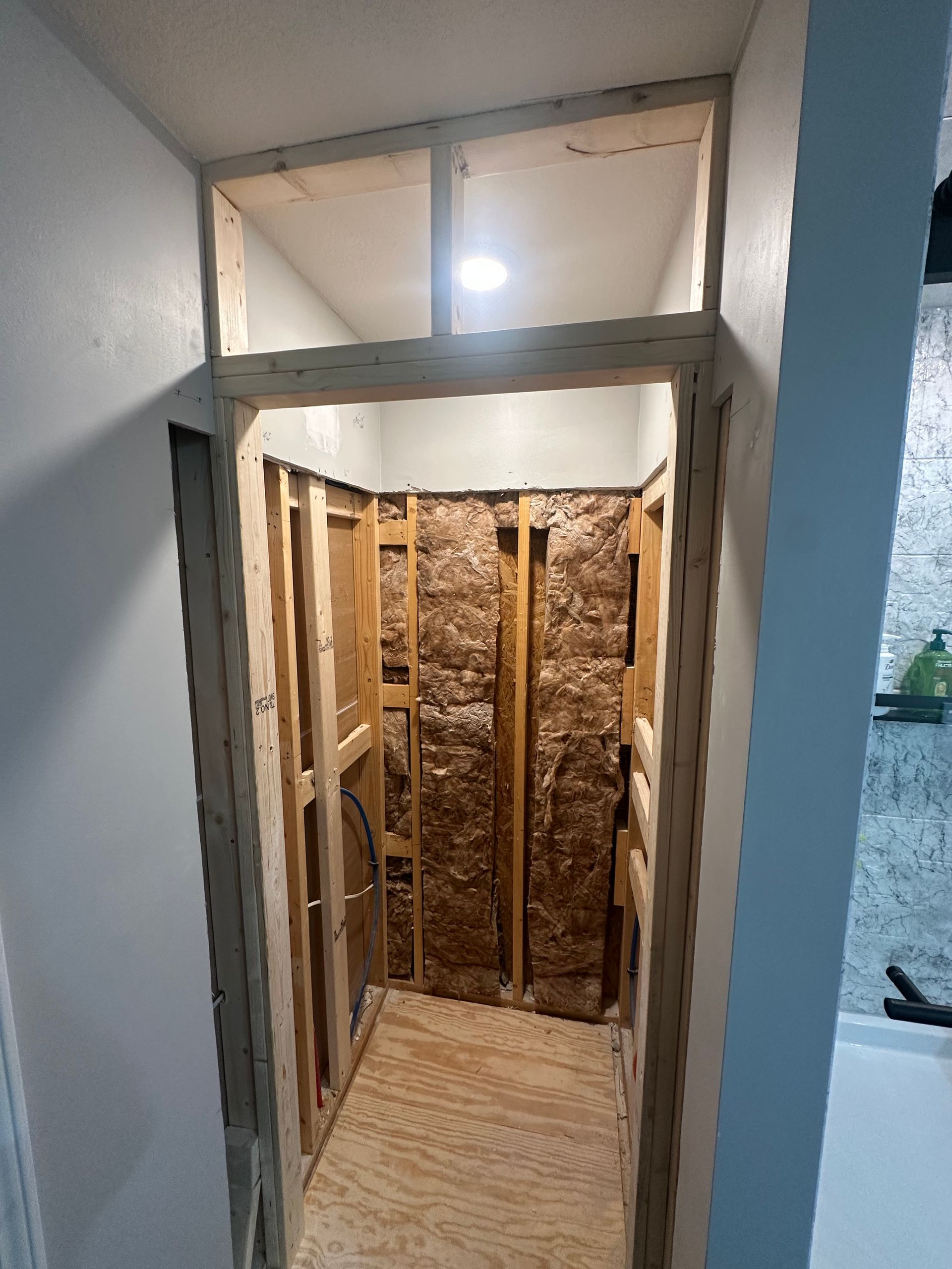 Framed shower stall under construction; wooden studs, insulation, and doorway.