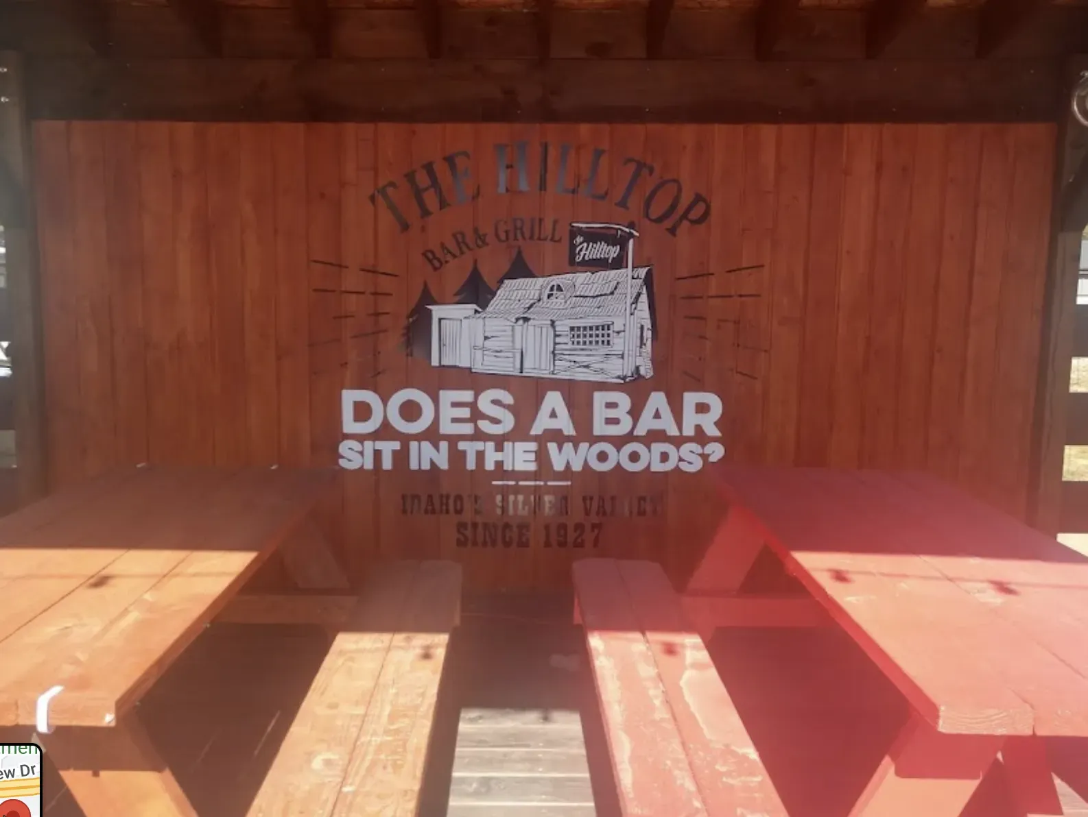 Outdoor seating at The Rooftop Bar & Grill. picnic tables under a wall with logo, and tagline 