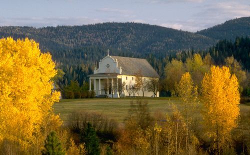 White building with columns, nestled in a valley, surrounded by golden autumn trees and forested hills.