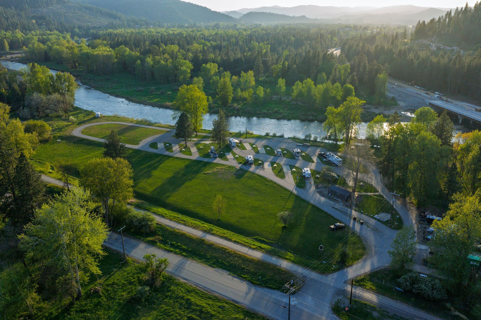 Aerial view of a green park with winding paths, parking lot, and river at sunset