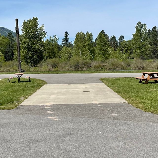 Campsite with concrete pad, picnic tables, and trees in background under a blue sky.