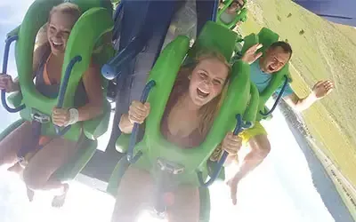 People screaming on a green and blue amusement ride, flying through the air.