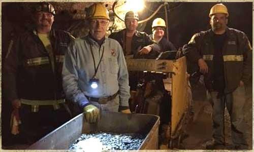 Five people in hard hats pose near mining equipment in a dark tunnel.
