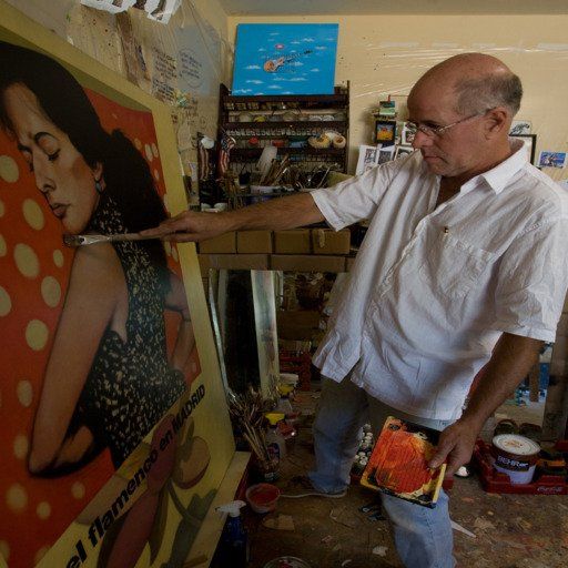 Artist measures a large painting of a woman in a polka dot background, holding a palette, in a cluttered studio.