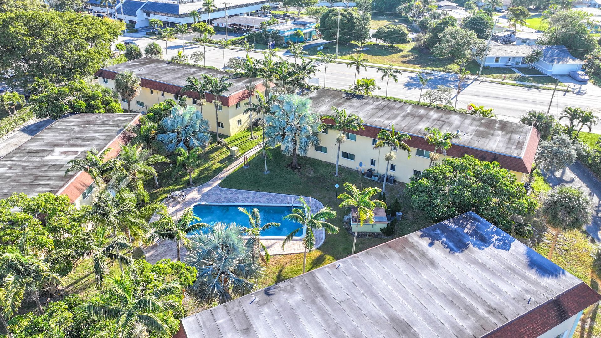 Photo of the apartment complex scene from a drone view, showing the pool and lush landscaping