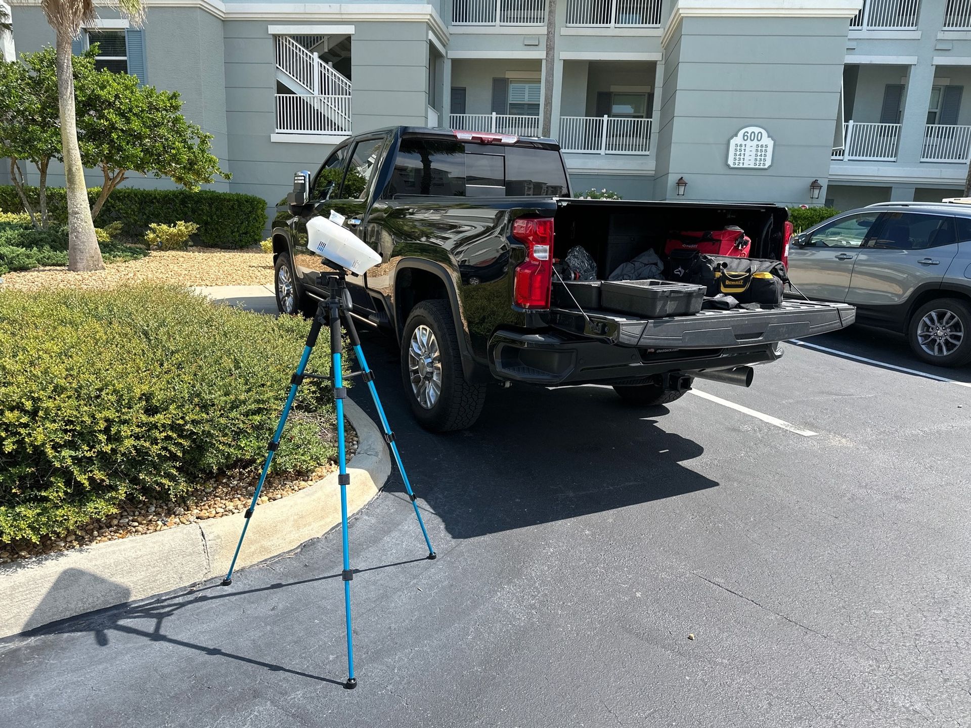 A black pickup truck parked in a lot with a white tripod-mounted device positioned near a bush.