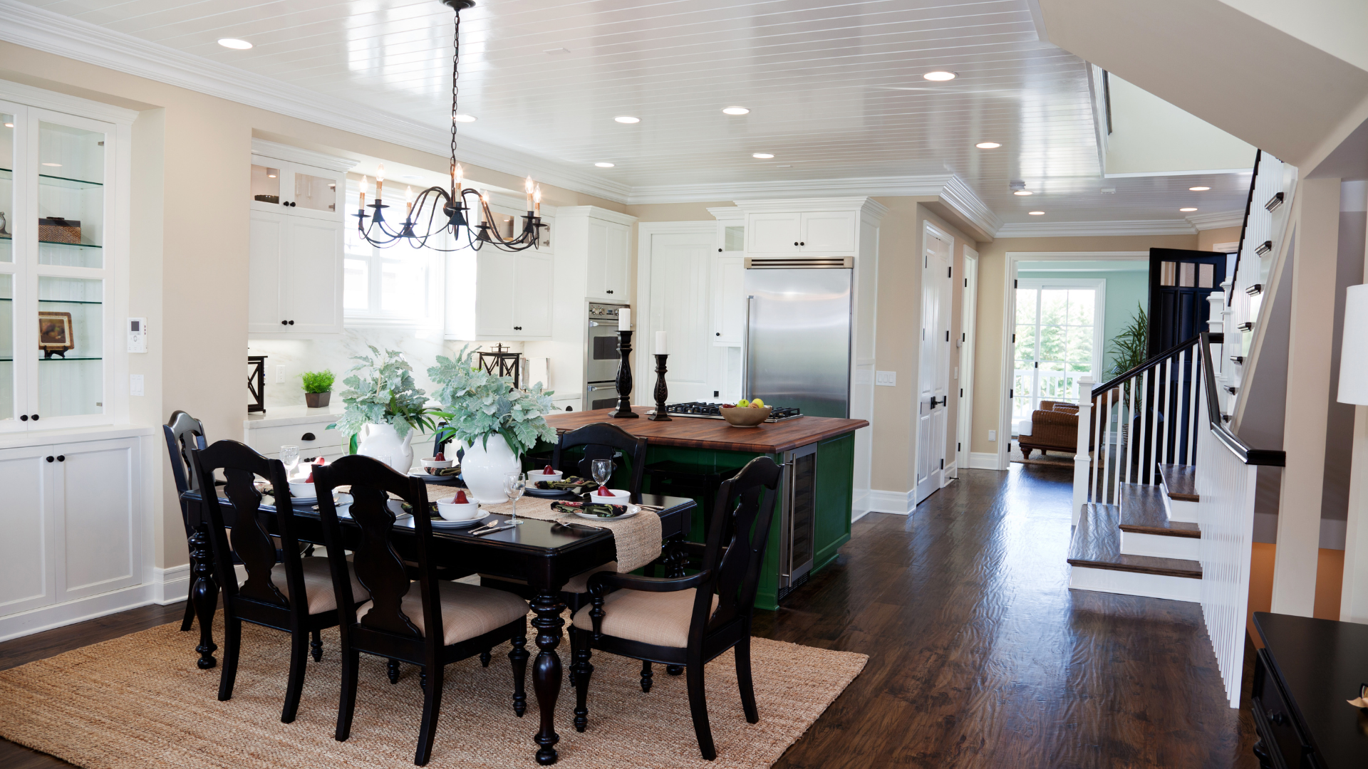 Dining room with a dark wood table and chairs, adjacent to a modern kitchen with a center island and hardwood floors.