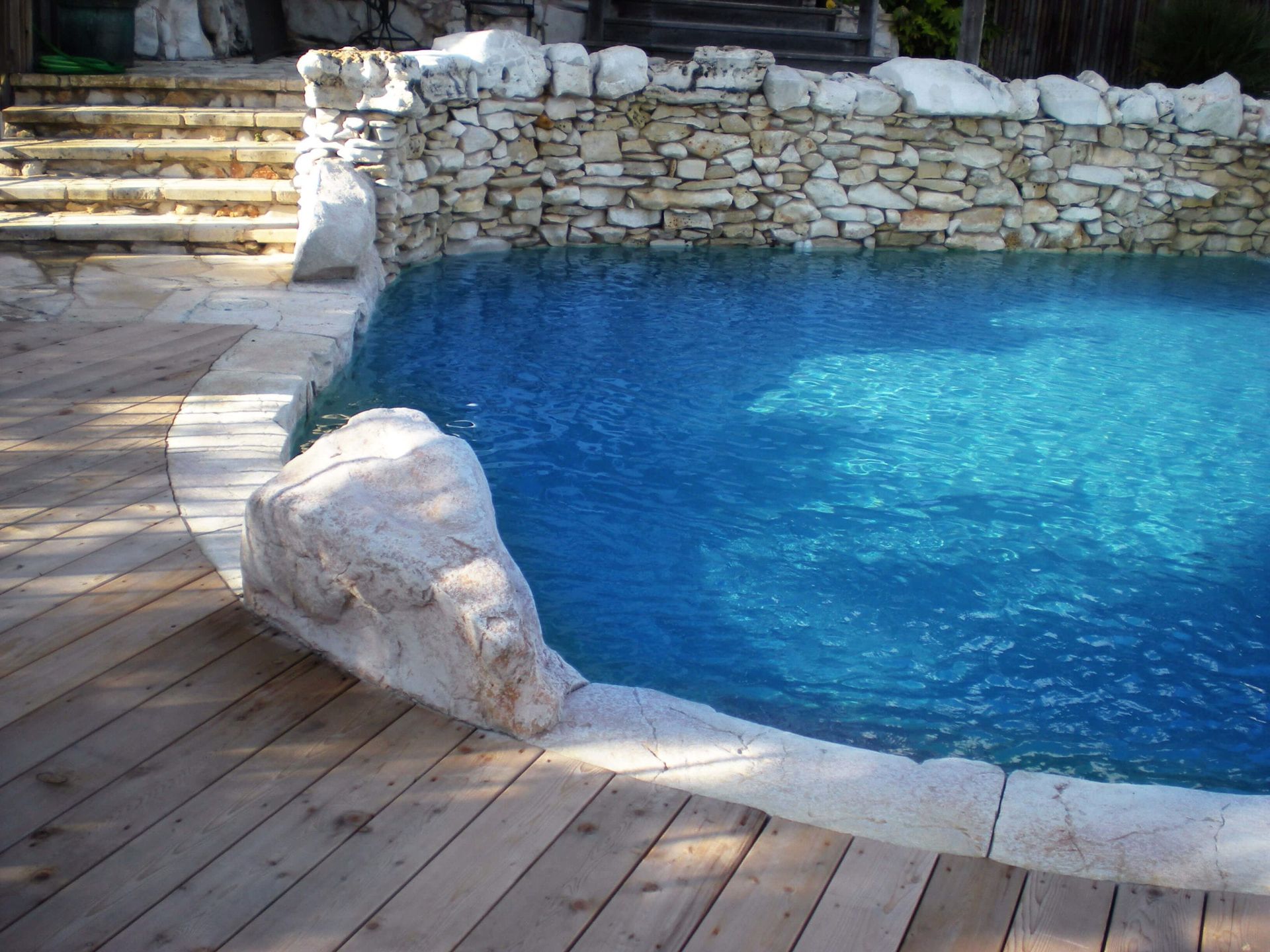 A large swimming pool surrounded by rocks and a wooden deck
