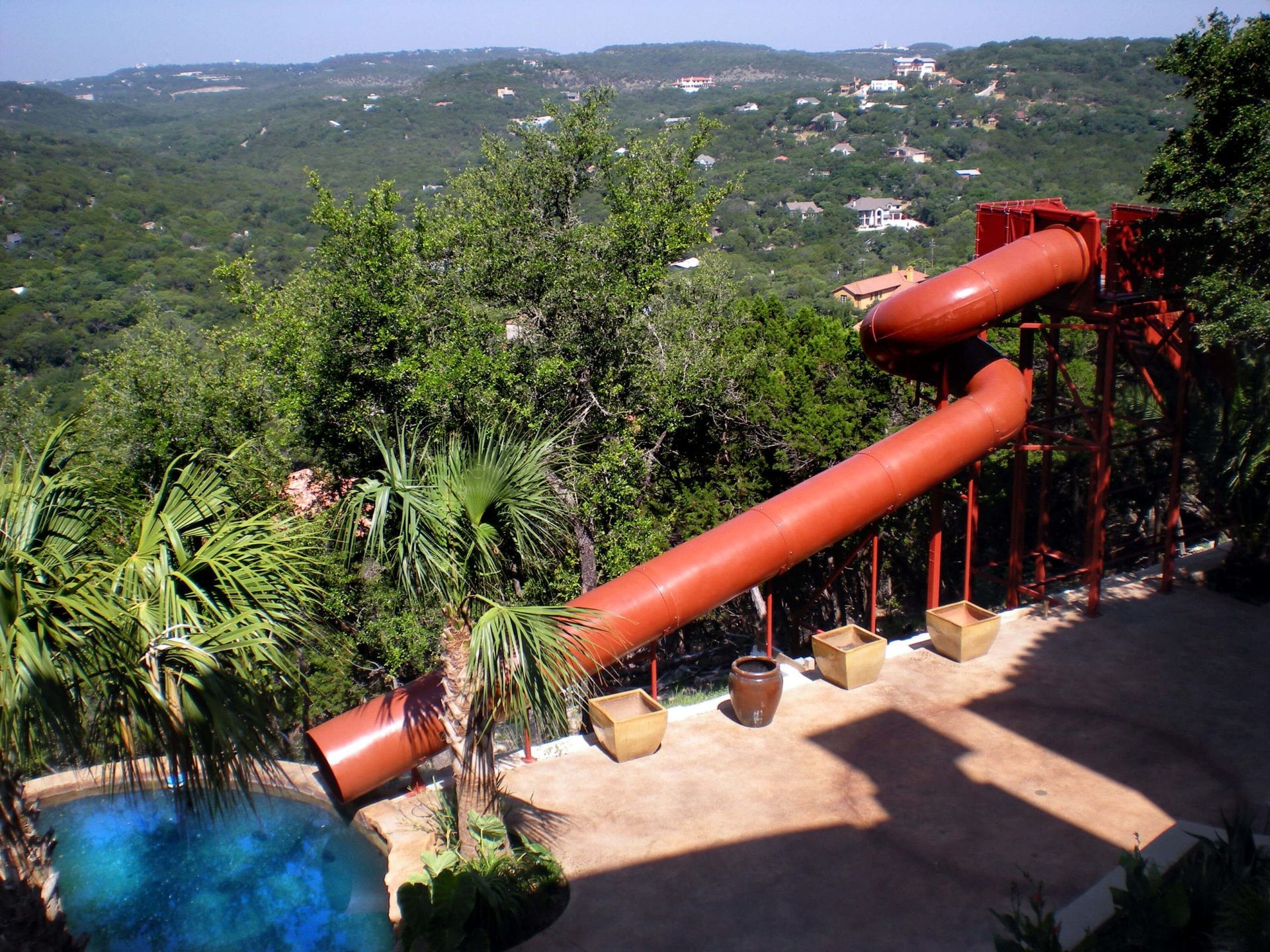 A large water slide is surrounded by trees and a pool