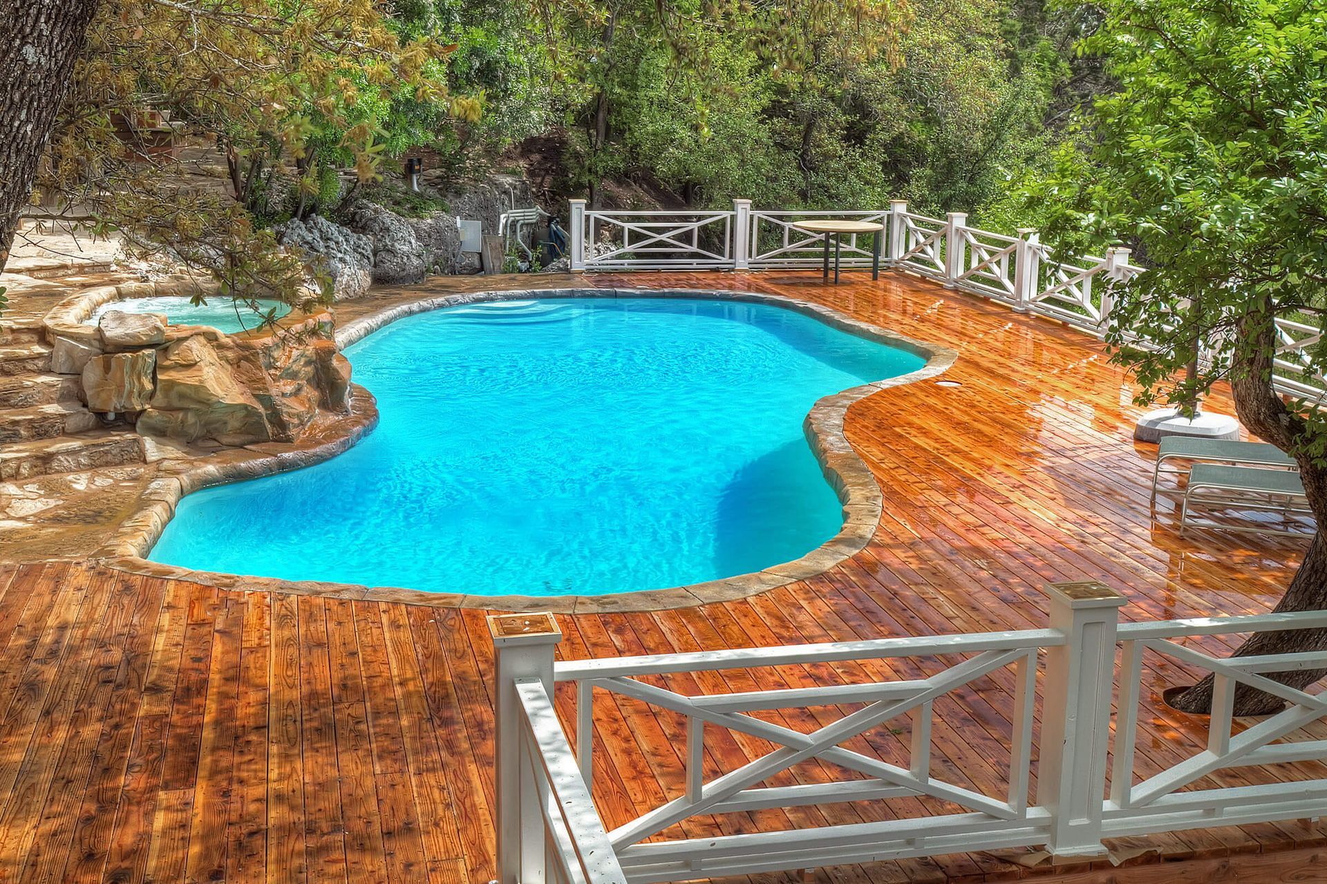 A large swimming pool surrounded by trees and a wooden deck.