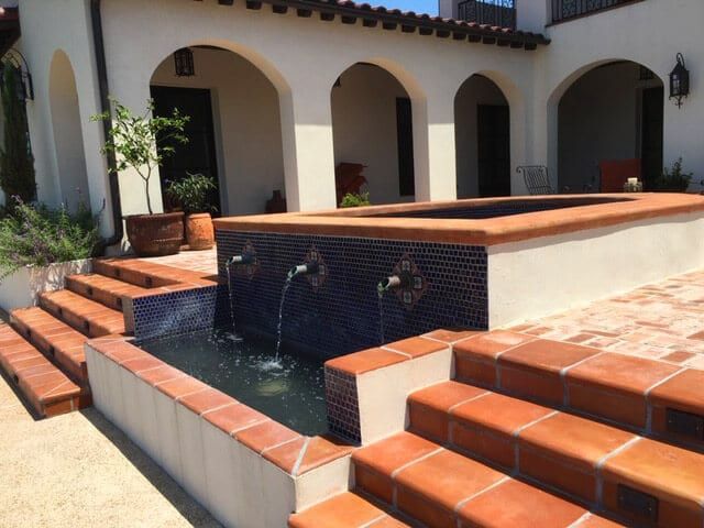 A fountain is surrounded by stairs in front of a house
