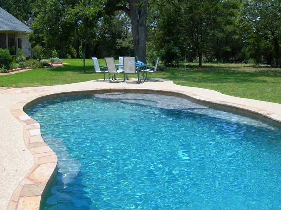A large swimming pool with a table and chairs in the background