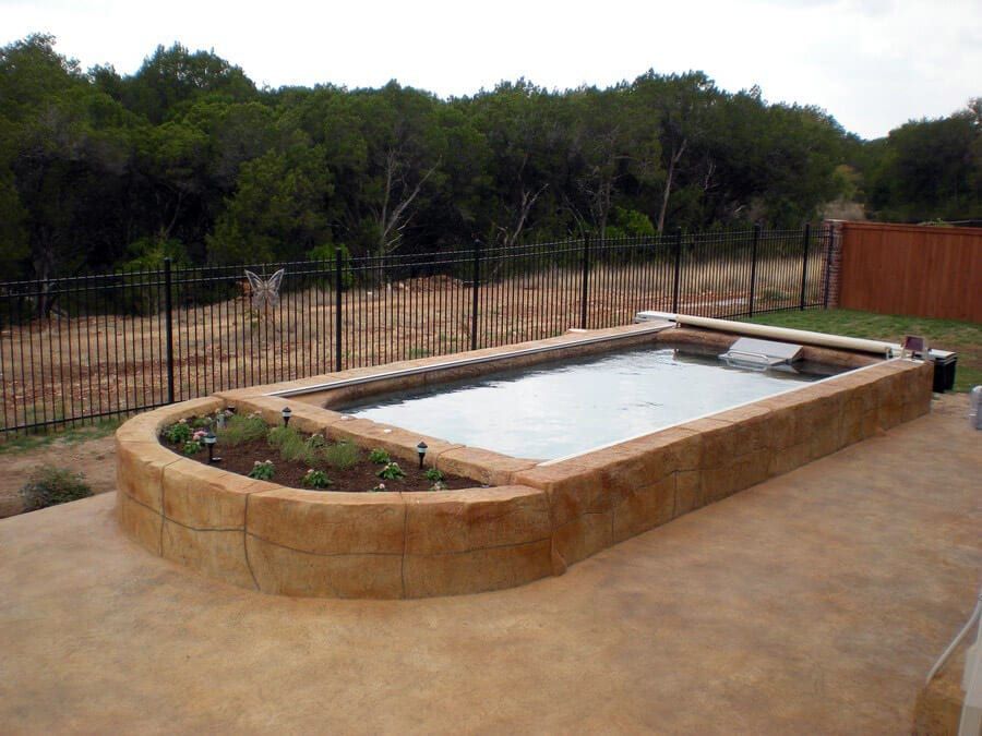 A large swimming pool is surrounded by a fence and trees.