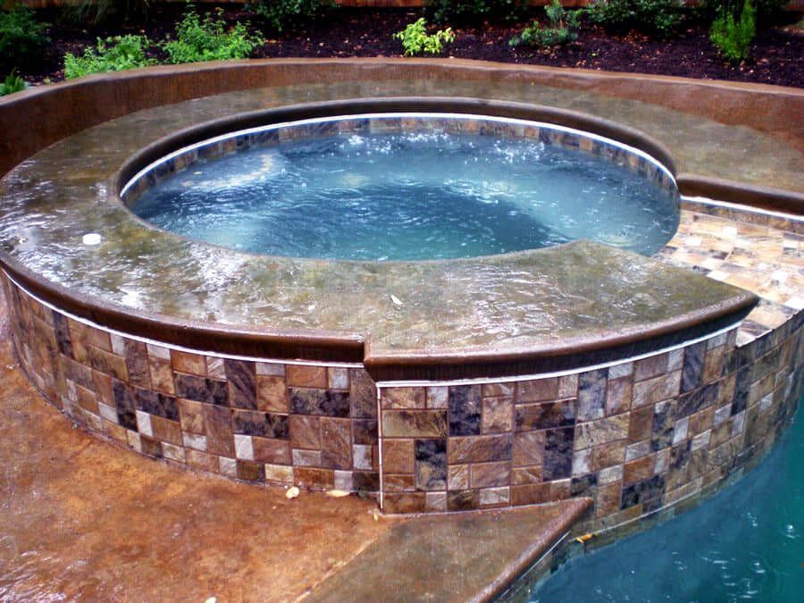 A hot tub is surrounded by a tiled wall next to a swimming pool