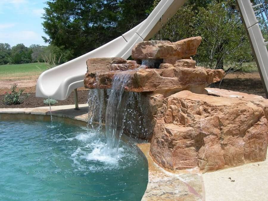 A water slide is next to a waterfall in a pool
