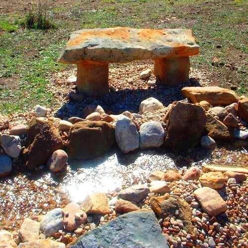 A stone bench is surrounded by rocks in a field