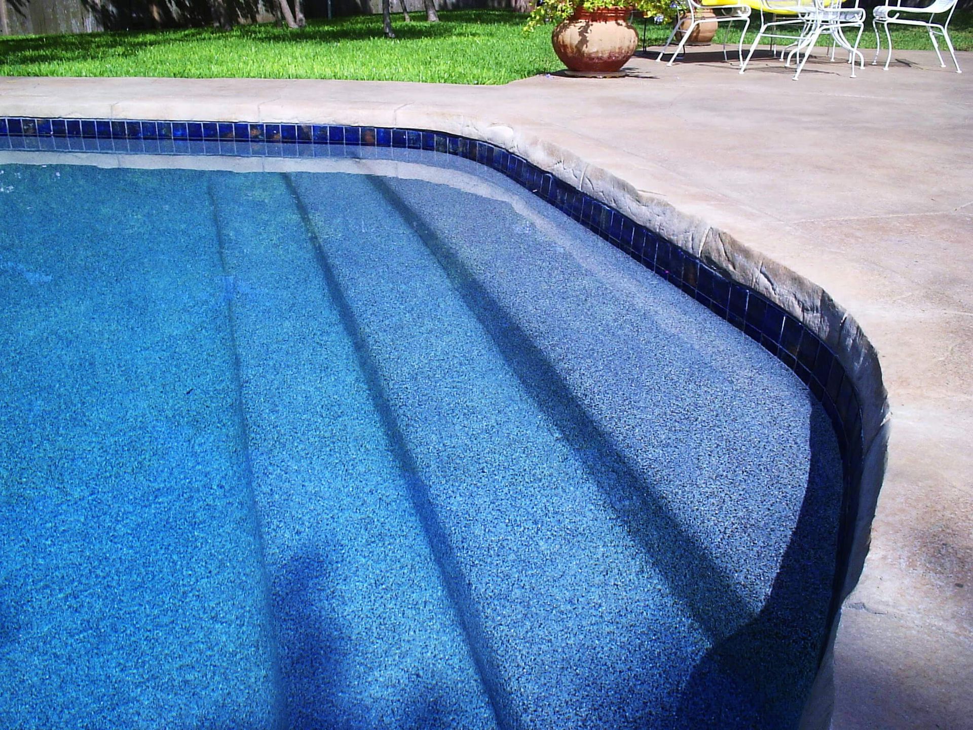 A swimming pool with stairs and a patio in the background