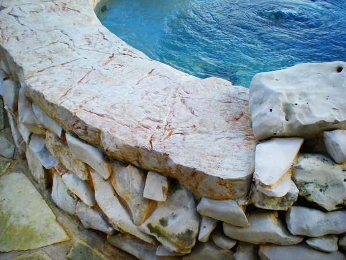 A stone wall surrounds a swimming pool with blue water