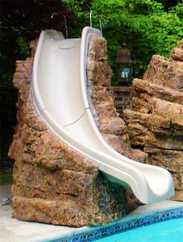 A slide is built into a rock wall next to a swimming pool.