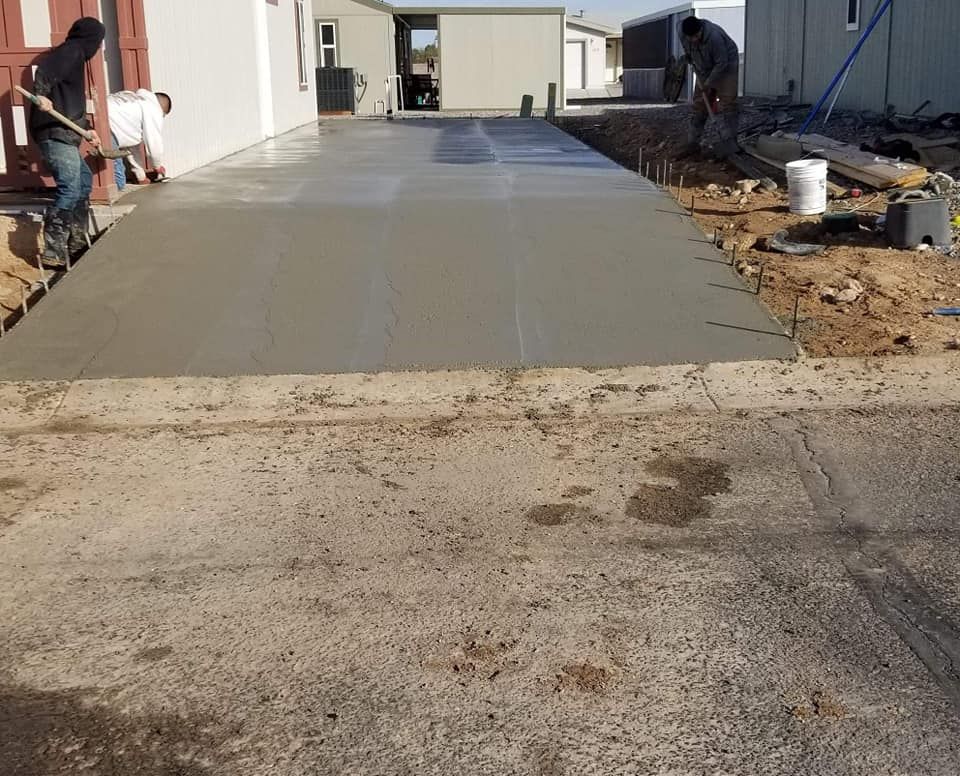 Two men are working on a concrete driveway in front of a house