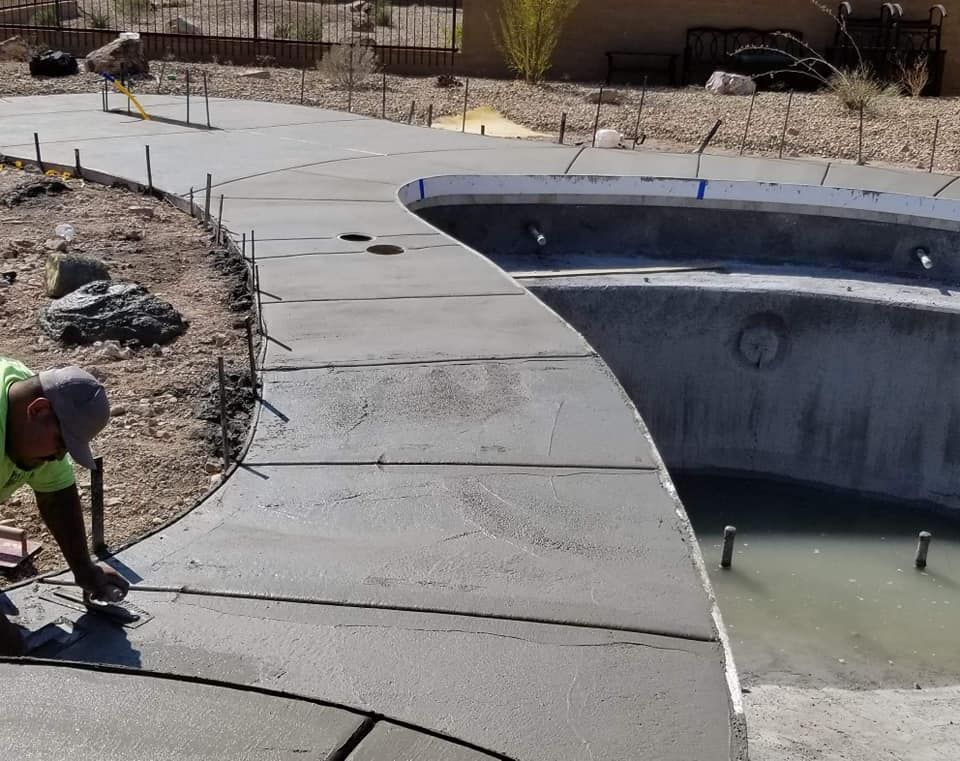 A man is working on a concrete walkway next to a pool