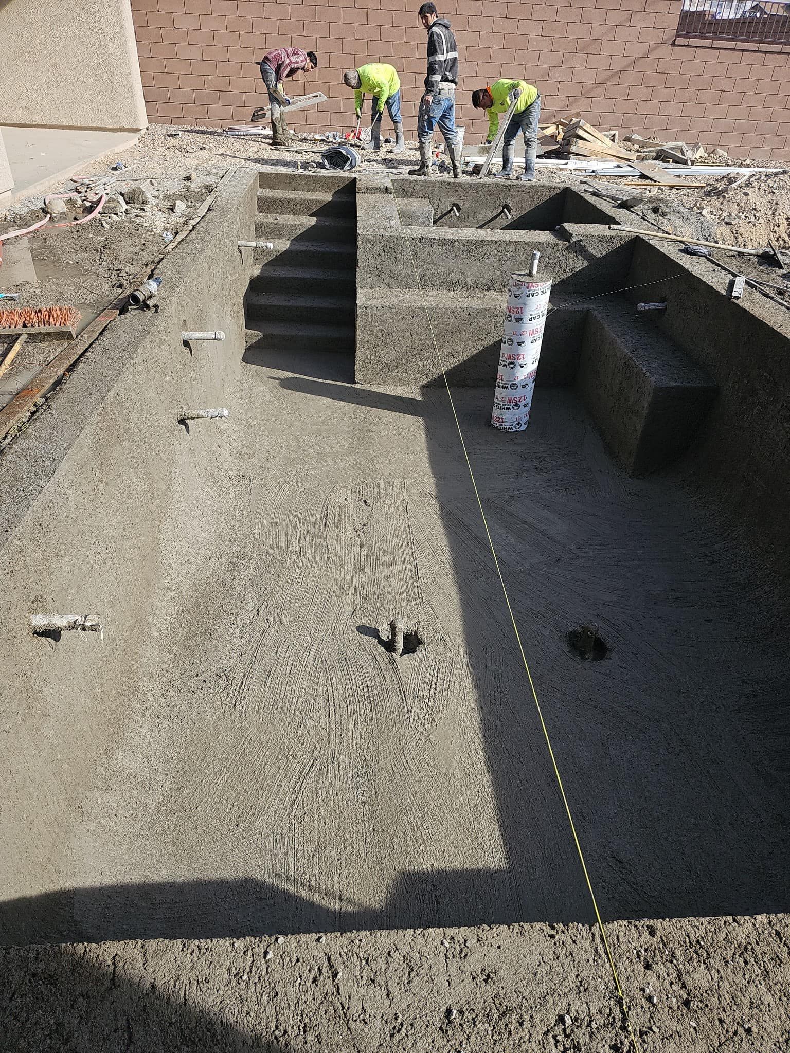 A group of construction workers are working on a swimming pool.