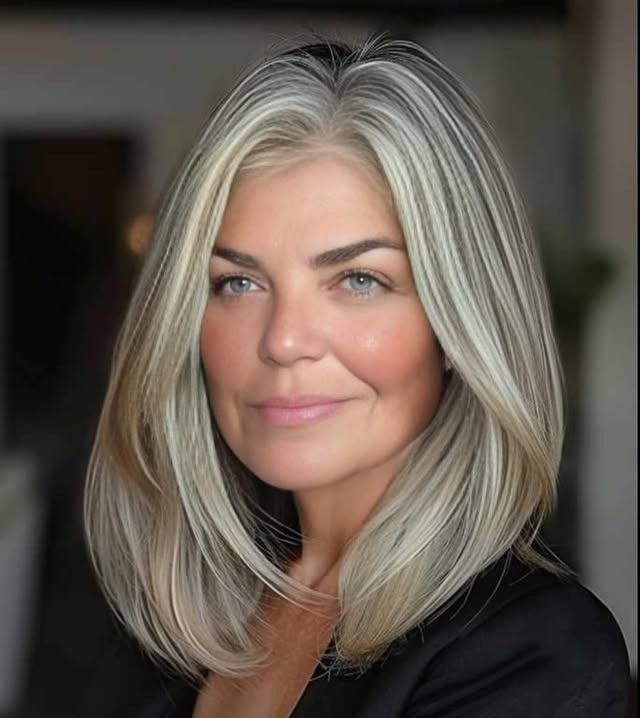A woman with gray hair is wearing a black jacket and smiling.