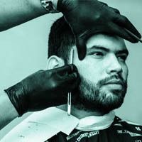 A man with a beard is getting his hair cut by a barber.