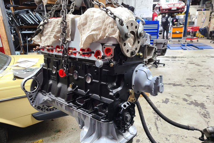 Engine block being lifted by a chain hoist in a repair shop. | Kraft German Auto