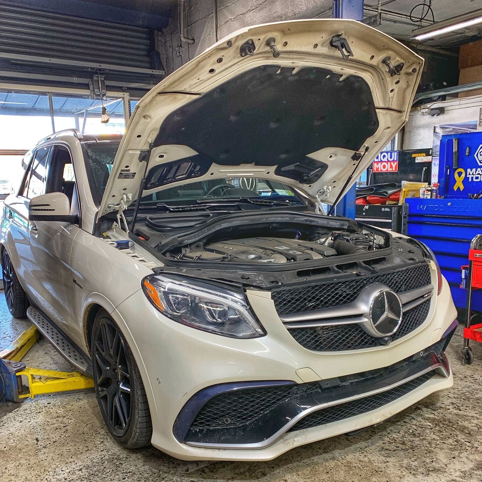 White Mercedes SUV with hood open in a repair shop, up on a lift. | Kraft German Auto