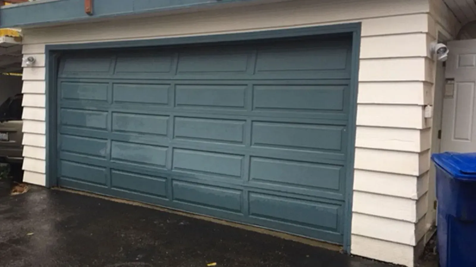 A blue, multi-panel garage door on a residential building with white horizontal siding.