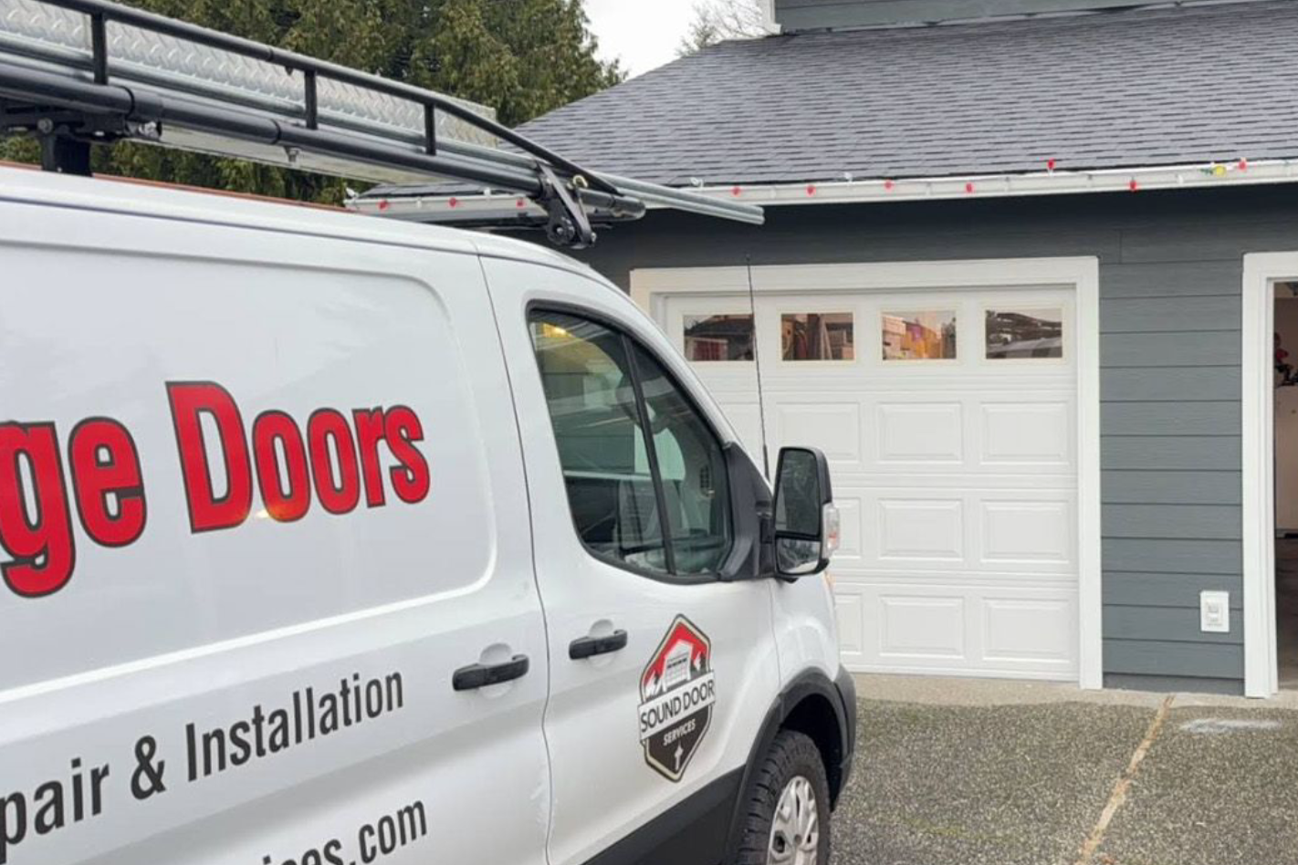 A white service van parked in front of a residential garage with a white sectional door.