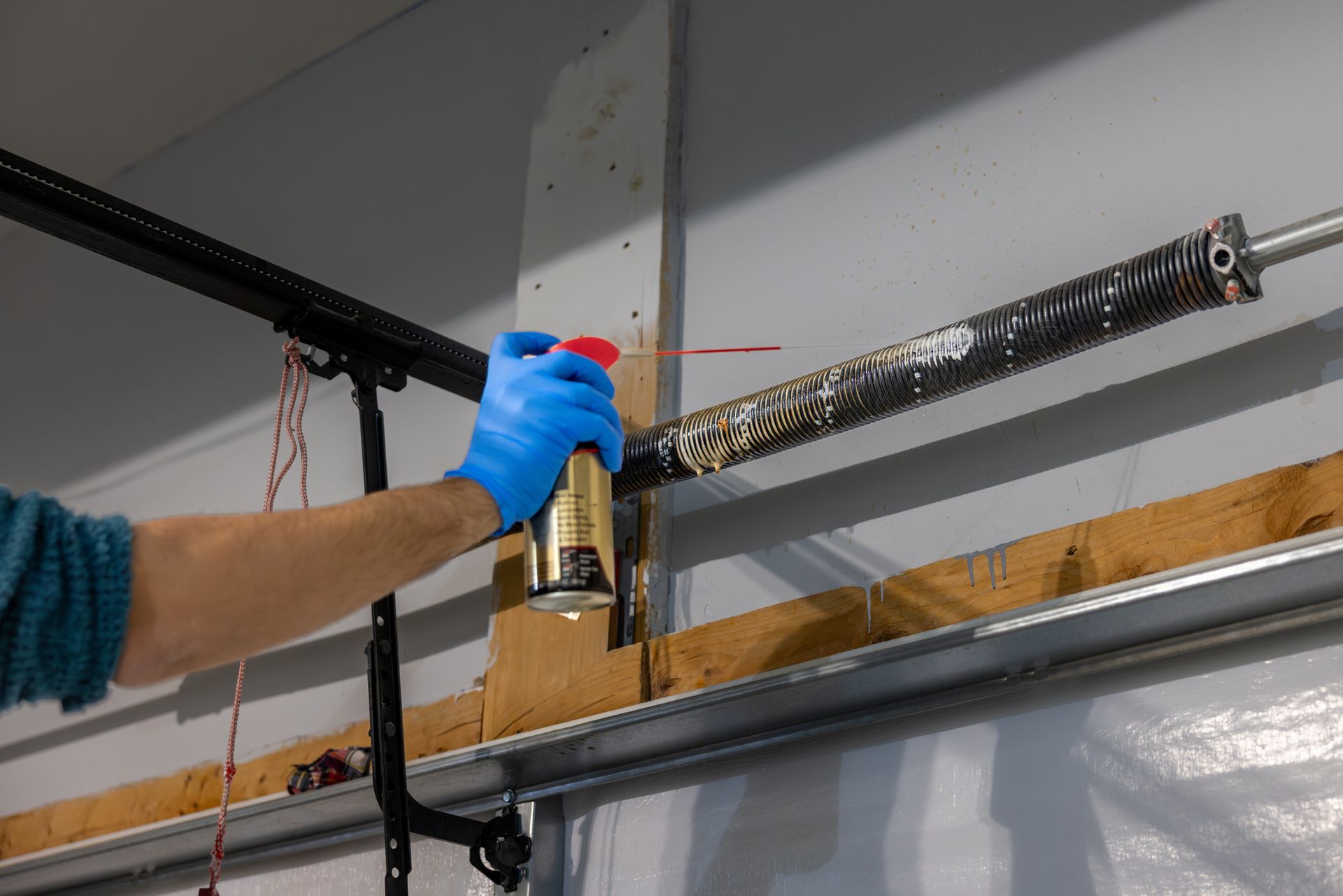 Sound Door Services technician sprays lubricant onto a metal garage door torsion spring.