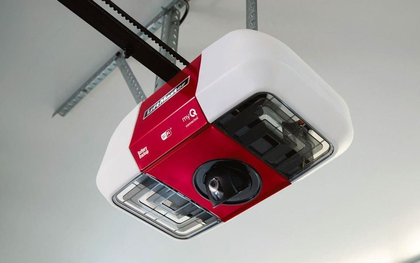 A white and red Chamberlin garage door opener mounted to a ceiling with an integrated camera and light.