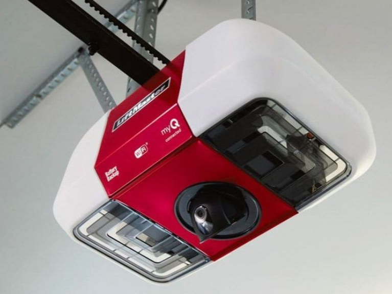 A white and red LiftMaster garage door opener with an integrated camera, mounted to a garage ceiling.