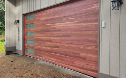 Modern wood garage door with a row of five frosted windows on the left side, mounted on a tan exterior wall.