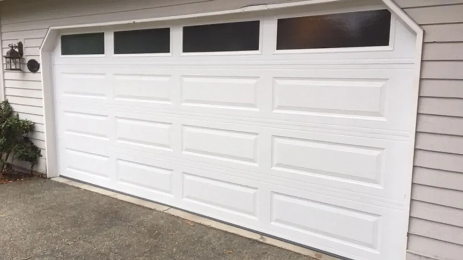 A white, four-panel residential garage door with a row of four rectangular windows across the top.